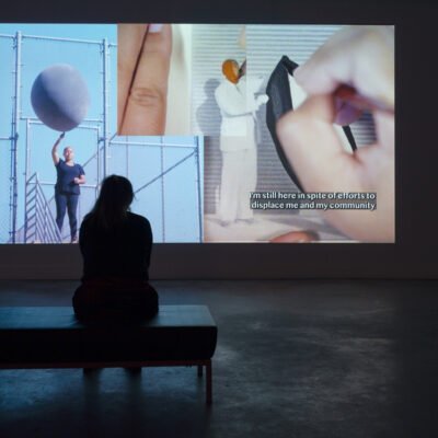 Person sitting in gallery watching A Welcoming Place, 2020-2022, digital video