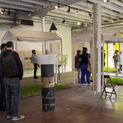 Installation view of fabric and wood hangings with grass panels on the ground.
