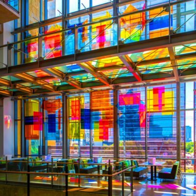 Colorful, clear block installation at the austin public library. hanging infront of a big window, the sun shines through the colorful panels.