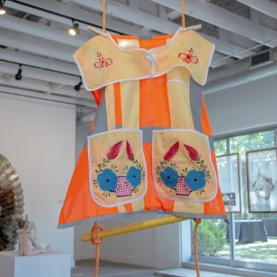 Close up of a decorated, high visibility workers vest hanging from a rope ladder. Titled Visible Labor by Angela Faz