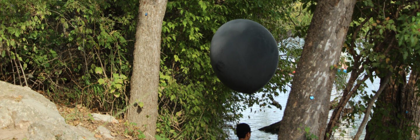 Production still of Ariel René Jackson sitting by trees holding black balloon, photographed by Hiram Mojica