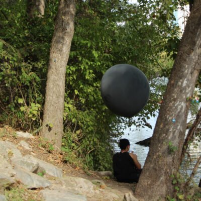 Production still of Ariel René Jackson sitting by trees holding black balloon, photographed by Hiram Mojica