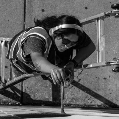 black and white photo taken from above of someone painting a wall mural while standing on a ladder by Deborah Cole