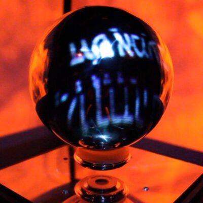 Still of a dark reflective orb against a bright orange background from Pillar of Cloud // Pillar of Fire (Fire) video installation
