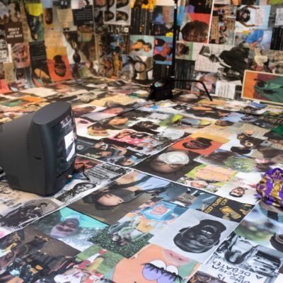 Photo of a room with the walls and floors covered in photographs of people, with an old box television sitting on the ground from Ciara Elle Bryant's Server_ A streamed revolution