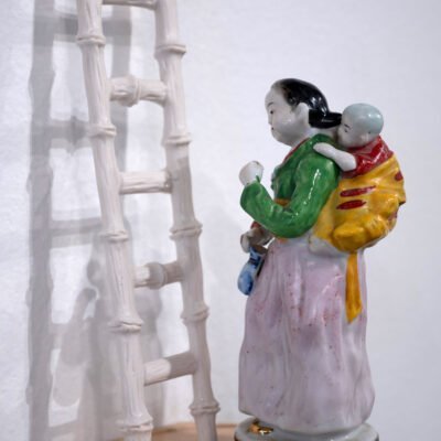 porcelain figurine of chinese woman in traditional clothing, carrying a baby on her back.