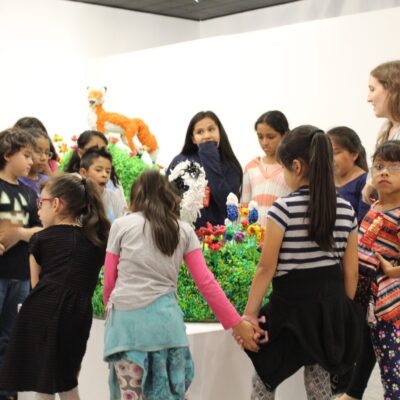 Children gathered around very colorful sculpture of grass and animals.